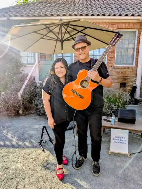 Laura Bravo with her guitarist and his orange guitar at an outdoor event