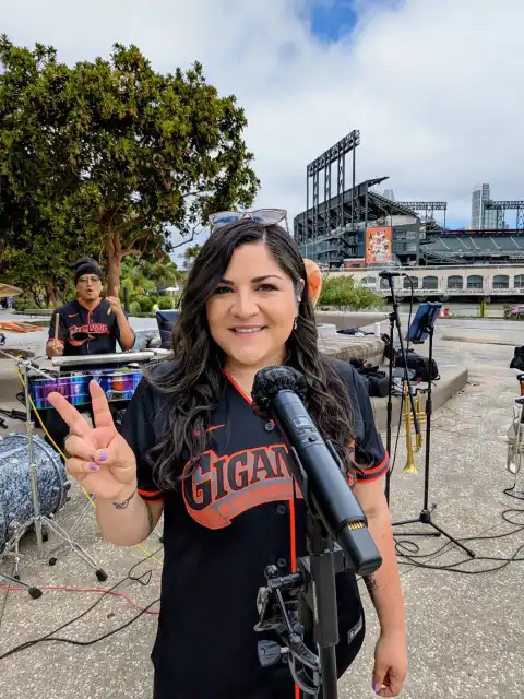 Laura Bravo in a Gigantes jersey giving a peace sign beside Oracle Park