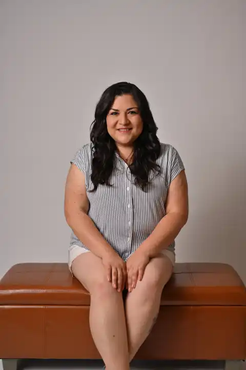 Laura Bravo seated on a leather bench in a studio portrait